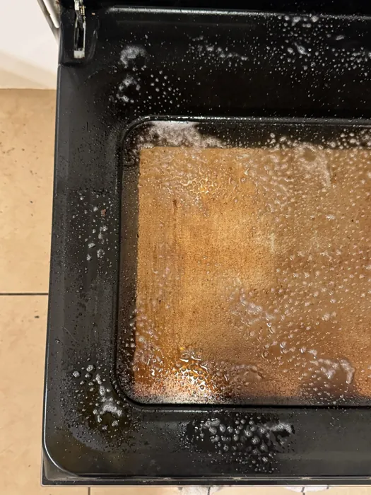 Oven tray coated in baked-on grease, soaking under cleaning foam before the work starts