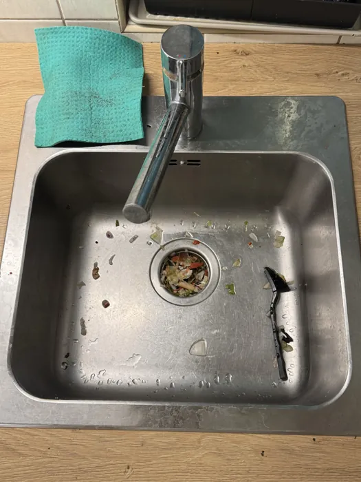 Kitchen sink before cleaning, food debris around the strainer
