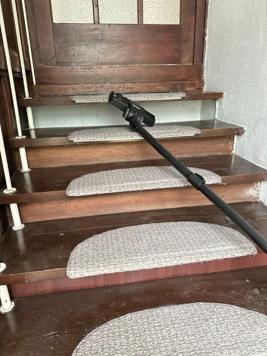 Extraction wand being drawn across a wooden staircase tread mid-clean, Budapest